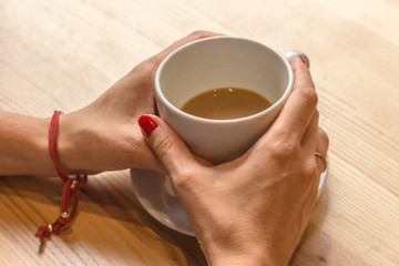 White cup of coffee in female hands. Warm your hands with a cup of hot drink. Meeting in a cafe....