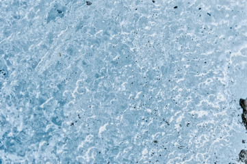 Fototapeta na wymiar A close-up of the surface of a fragment of a glacier with a structure of strips and bubbles interspersed with sand and rocky rock. Ice blue texture to the light. Small DOF