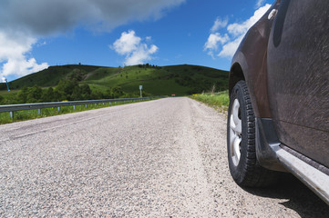 Close-up of a SUV wheel on an asphalt road outside the city against the green hills of blue sky and clouds