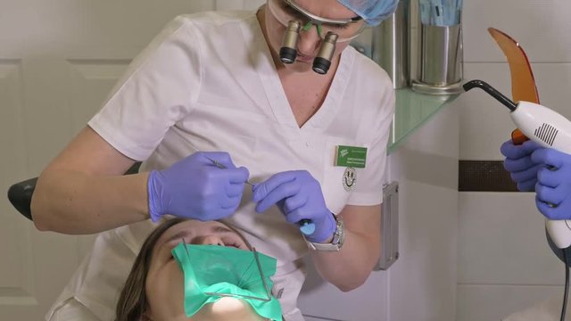 Woman at dentist clinic gets dental treatment to fill a cavity in a tooth. Dental restoration and composite material polymerization with UV light and laser. The doctor works with an assistant.