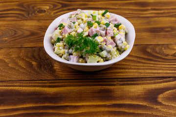 Tasty salad with sausage, green pea, canned corn, bell pepper, cucumber and mayonnaise on wooden table