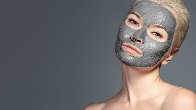 Beautiful Woman Applying Black Facial Mask. Beauty Treatments. Spa Girl Apply Clay Facial mask on grey background