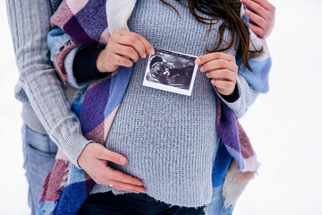 Close up man holding woman's pregnant belly and the woman holding ultrasound pregnancy picture in...