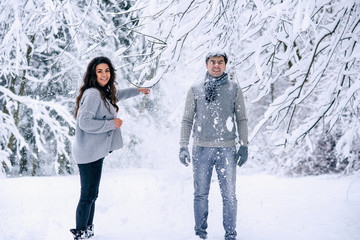 Fototapeta na wymiar Happy beautiful pregnant woman in warm clothes throws snow on her husband. Couple in love having fun in winter park.