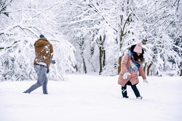 Fototapeta na wymiar Loving young couple playing with snowballs in a winter park. Family love and care concept.
