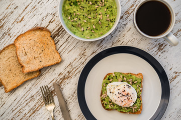 Food photography of an avocado toast with poached egg, sesame seeds, and black coffee. Breakfast, lunch, brunch, light dinner dish meal, vegetarian food, healthy eating concept.