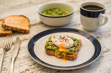 Food photography of an avocado toast with poached egg, sesame seeds, and black coffee. Breakfast, lunch, brunch, light dinner dish meal, vegetarian food, healthy eating concept.
