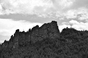Fototapeta na wymiar Black and white photo of mountains and rocks. The mountains are covered with dense forests, a small rock rises on top of the hill.