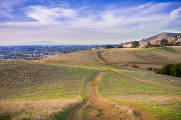 Hiking trail over the hills of Garin Dry Creek Pioneer Regional Park at sunset, Oakland and San Francisco skyline in the background, California