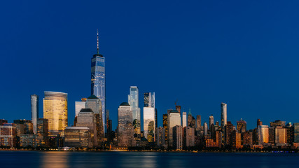 Night view of skyline of downtown Manhattan over Hudson River under dark blue sky, in New York City, USA
