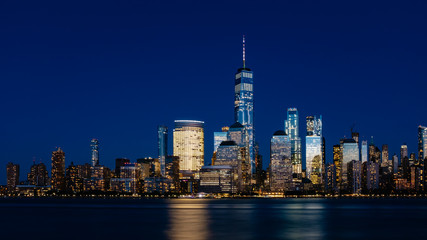 Fototapeta na wymiar Night view of skyline of downtown Manhattan over Hudson River under dark blue sky, in New York City, USA