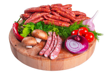 Hunting smoked sausages isolated on white background. Sausage with greens and vegetables on a wooden round board