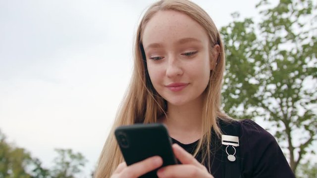 An attractive young red-haired lady using a phone in town. Close-up shot. Soft focus