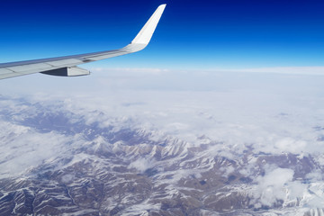 Naklejka na ściany i meble Wing of an airplane flying above the snow mountains in Southwest China. The view from an airplane window. Travel concept.