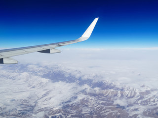 Obraz premium Wing of an airplane flying above the snow mountains in Southwest China. The view from an airplane window. Travel concept.
