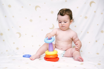Fototapeta premium Baby in a diaper sitting and playing a colorful pyramid