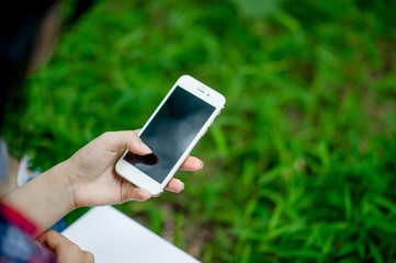 Girl playing phone on hand for online communication and contact Wear red shirt and green background And there is a copy space.