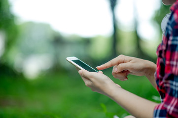 Girl playing phone on hand for online communication and contact Wear red shirt and green background And there is a copy space.