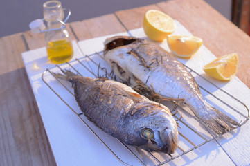 grilled dorado fish on a grill grate with lemon and olive oil bottle