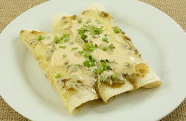 Chicken and bean salsa verde enchildas on plate with cheese and chopped green onions