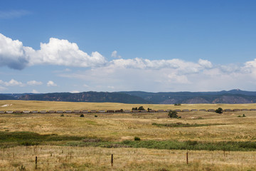 Obraz premium Scenic mountains, clear deep sky with white clouds on a summer sunny day. At the foot of the mountains are located houses of small American cities. Colorado, USA.