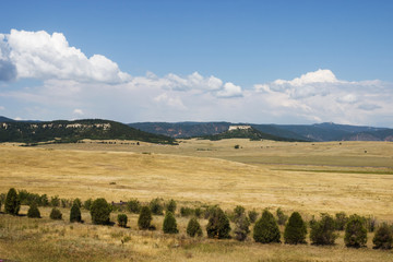 Obraz premium Scenic mountains, clear deep sky with white clouds on a summer sunny day. At the foot of the mountains are located houses of small American cities. Colorado, USA.
