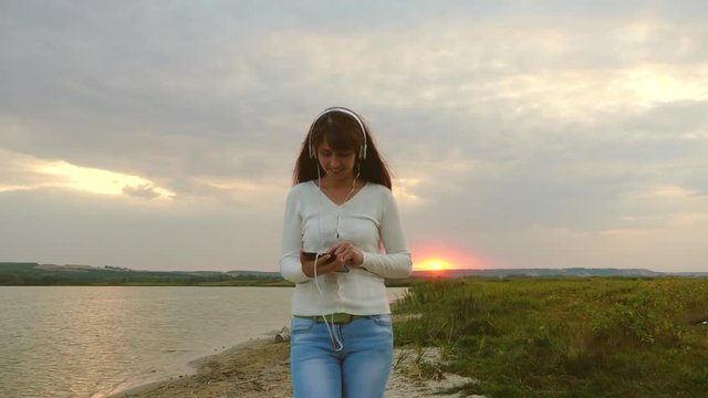 beautiful girl in headphones walks on beach with tablet and is video conferencing online