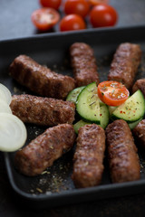 Barbecued cevapcici or skinless beef sausages with cucumber, tomatoes and onion, closeup, selective focus