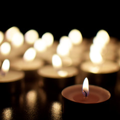 Round tea light candles burning in darkness. Advent or memorial prayer candle flame.