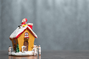 Miniature people painting house and Santa Claus sitting on the roof