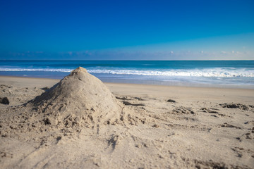 Fototapeta na wymiar sand castle on white sand beach meet tropical ocean with small waves and nice blue sky background in Summer - Ocean City, Maryland USA