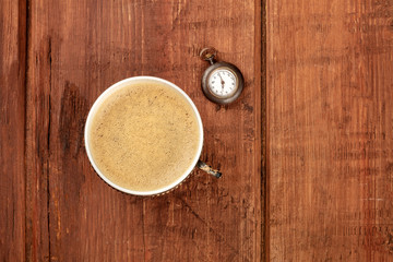 A cup of coffee and a vintage watch showing 7 o'clock, shot from the top on a dark rustic wooden background with a place for text