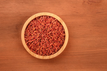 Camargue red rice, shot from the top in a wooden bowl on a dark rustic background with a place for text