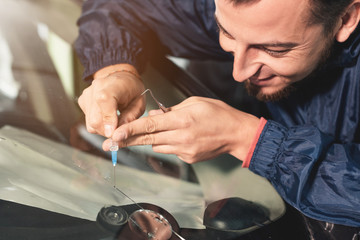 Close-up of a professional windshield repairman fills a crack in the glass with a special polymer through a syringe. Elimination of cracks and chips on windshields