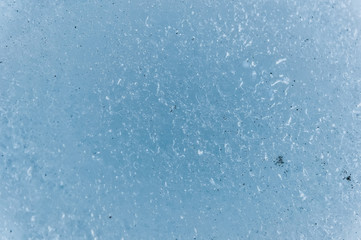 A close-up of the surface of a fragment of a glacier with a structure of strips and bubbles interspersed with sand and rocky rock. Ice blue texture to the light. Small DOF