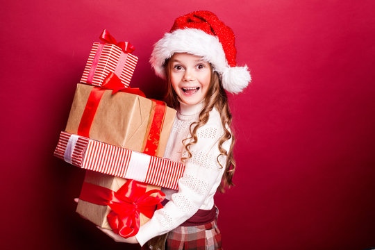 Happy smiling girl in a Christmas cap with a stack of red and brown gift boxes on the red background. Merry Christmas. Black Friday. Sale. Shopping
