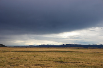 Obraz premium Summer day, dark sky, big dark blue clouds in the sky. In the steppe before the rain. Dark blue mountains on the horizon