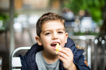 Fototapeta premium Little kid eating a chip seated on a bar
