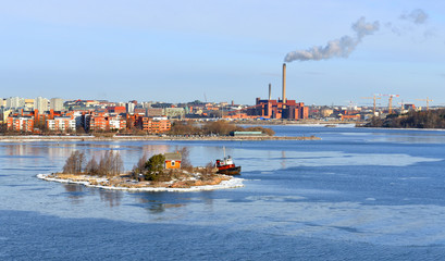 Small rocky island of Helsinki archipelago against  backdrop of industrial area of city. Finland