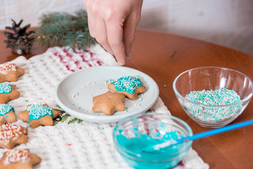 Preparing for Christmas, decorating traditional gingerbread with multicolored sugar glaze, the girl folds the cookies in a white gift box, with ribbon bow, on a white marble table copy space top view