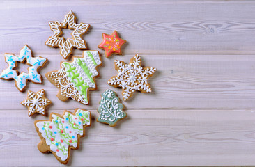 Fototapeta na wymiar Various colorful Christmas gingerbread in the shape of a Christmas tree and in the shape of a star decorated with green and red icing on a wooden white board with free space on right side 
