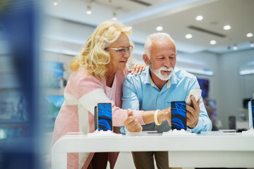 Senior couple choosing smart phone. Tech store interior.