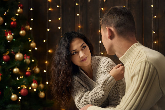 young couple in christmas lights and decoration, dressed in white, fir tree on dark wooden background, winter holiday concept