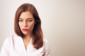 Obraz premium Portrait close-up of adult depressed sad woman in white blouse red lipstick hair loose looking down shooting on white background
