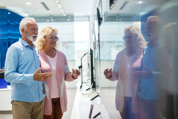 Happy senior couple choosing which television set to buy. Tech store interior.