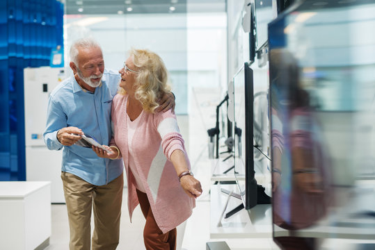 Happy senior couple choosing which television set to buy. Tech store interior.