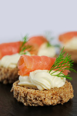 Smoked salmon canapes with cheese cream and dill on brown bread over black slate platter