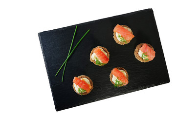 Smoked salmon canapes on black slate platter isolated on white background