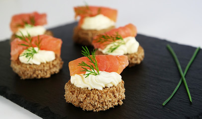 Smoked salmon canapes with cheese cream and dill on brown bread over black slate platter