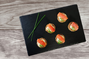 Smoked salmon canapes with cheese cream and dill served on black slate platter